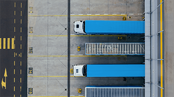Aerial view of three blue trucks parked parallel in designated spaces at a small-business-shipping-hubs loading dock. Yellow lines and numbers neatly mark the parking spots on the concrete surface.