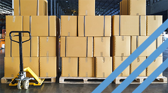 Stacks of brown cardboard boxes on wooden pallets in a warehouse. A yellow hand pallet truck is positioned in front of the boxes. Blue diagonal lines are overlaid on the right side of the image.