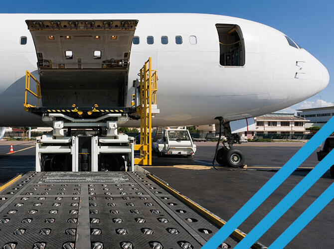 A white cargo airplane, ready for international freight, sits on the runway with its side compartment open. A loading mechanism is poised to transfer goods, framed by a clear blue sky and airport buildings. Blue diagonal lines grace the right side of the image.