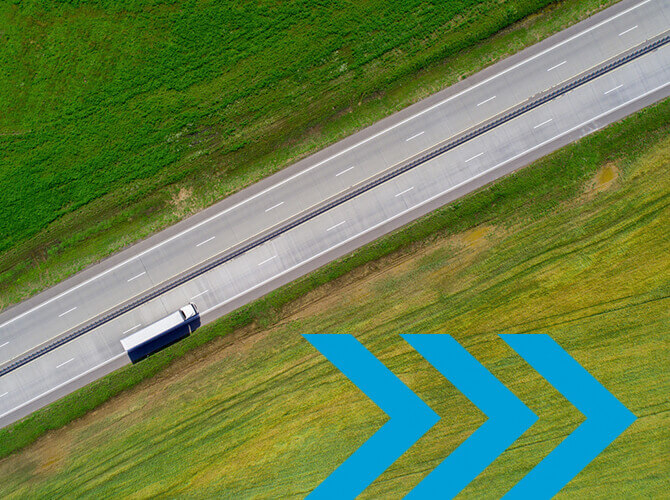 Aerial view of a road with a white and blue truck engaged in truckload shipping. Surrounding the road are green and yellow fields. In the foreground, three large blue arrows point to the right, overlaying part of the fields, as if quoting a journey through natures vibrant pages.