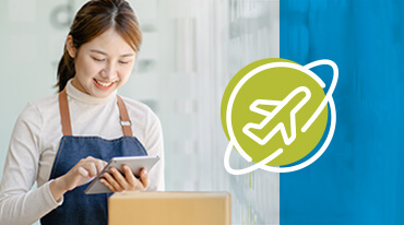 A person in a white turtleneck and apron smiles while using a tablet. Next to them is an icon of an airplane surrounded by a circular outline, set against a green circle on a blue background. A cardboard box is partially visible.