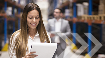 A woman with long hair smiles while holding a clipboard in a bustling small-business shipping hub. She is wearing a white shirt. In the blurred background, a person in a suit stands among shelves filled with boxes. Overlaying arrows point to the right.