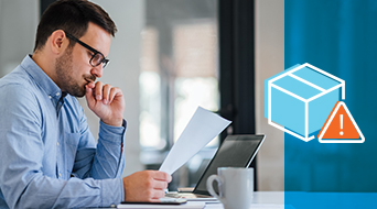 A man in a blue shirt and glasses is sitting at a table, looking at a piece of paper. A laptop and a white coffee mug are on the table. On the right, there is a blue overlay with an illustration of a box and a warning triangle.