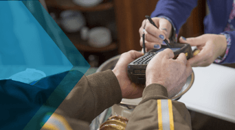 A person signs a handheld device held by another in a brown UPS SurePost uniform with yellow stripes. Indoors, with blurred objects in the background, the individual in the purple shirt completes the delivery process efficiently.