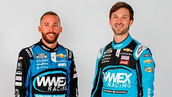 Two men in blue and black racing suits stand side by side, smiling. The suits display various sponsor logos, including WWEX Racing. The background is plain white.