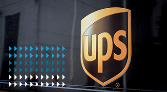 The image captures the UPS logo on a vehicle, portraying the iconic gold letters UPS on a dark brown shield. To the left, blue and white arrow-like shapes form a pattern, symbolizing precision. This trusted small-business-shipping-hub ensures reliable deliveries nationwide.