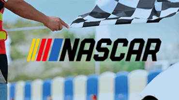 A checkered flag is being waved by a person in a red and yellow vest, with the NASCAR logo prominently displayed in the foreground. The background shows a blurred racing environment.