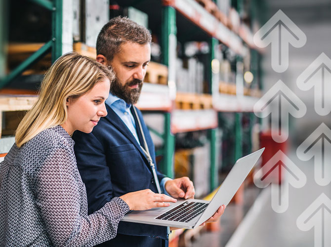 A man and a woman, both in business attire, are focused on a laptop in a 3PL warehousing setting. The woman types as shelves with boxes line the background. Transparent upward arrows overlay the scene, emphasizing growth or progress.