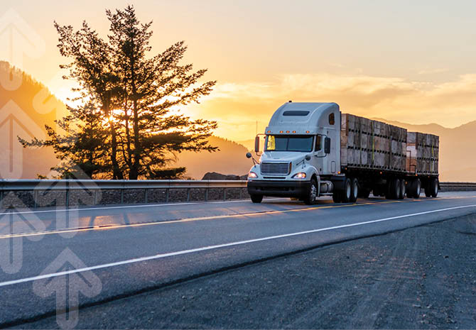 A large white semi-truck, part of a managed transportation fleet, drives along a highway with its cargo-laden trailer. The sun sets gracefully, casting a warm glow over a tree and distant mountains while faint arrows appear on the left side of the scene.