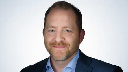 A man with short hair and a beard, resembling Daniel Curling, CTO of WWEX Group, is wearing a blue collared shirt and a dark suit jacket. He smiles slightly while looking directly at the camera against a plain, light background.