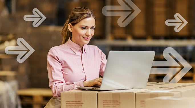 A woman in a pink shirt works on a laptop placed on stacked cardboard boxes in a warehouse. Transparent arrows pointing right are overlaid on the image, suggesting fast processing or movement.