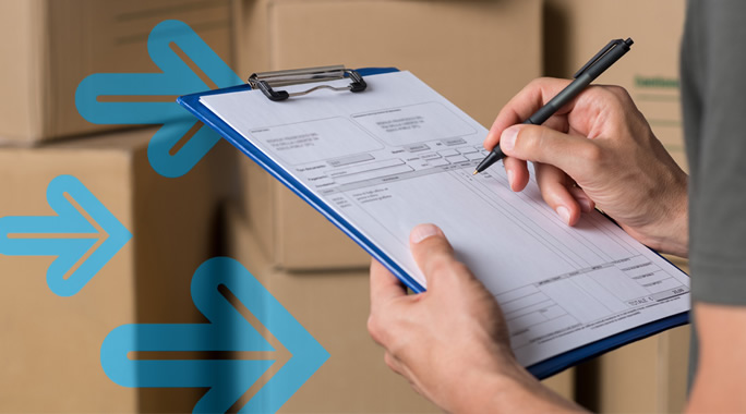 Person holding a clipboard, filling out a form with a pen. The background shows stacked cardboard boxes. Blue arrows are overlaid on the image, pointing to the left.