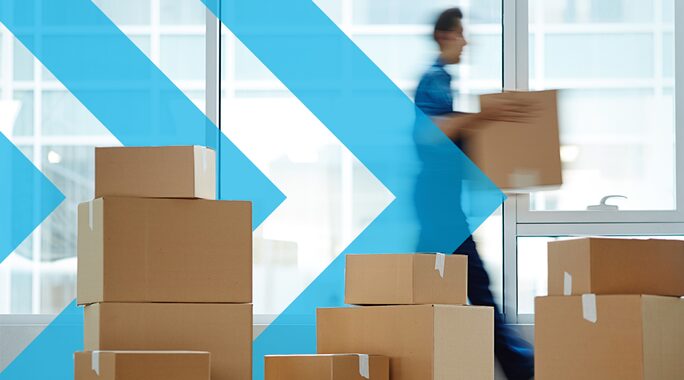 A person carrying a box walks past several stacked cardboard boxes. The background features large windows with a blue arrow graphic overlayed, suggesting movement or direction.