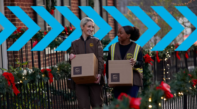Two UPS workers, one in uniform and the other in a reflective vest, carry boxes adorned with UPS logos. Theyre walking along a decorated street with greenery and red bows, showcasing the hustle of holiday shipping. Blue arrow graphics overlay the image, pointing right.