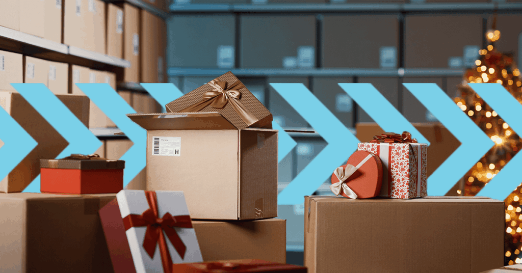 A stack of gift-wrapped boxes in a warehouse setting with large blue arrows pointing right. Some boxes have bows and festive wrapping, while the background shows shelves of plain boxes and a decorated Christmas tree.